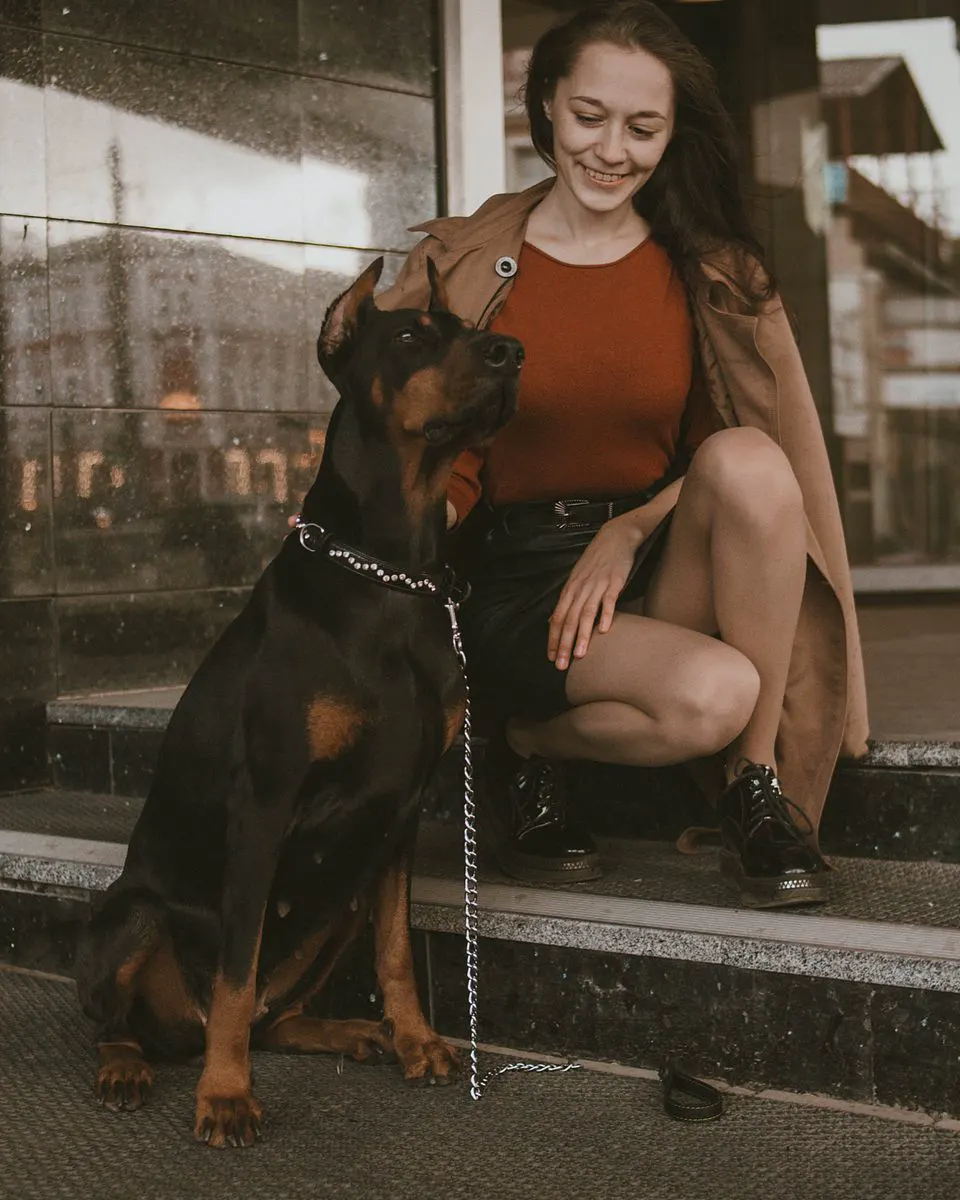Žena čuči na stepenicama pored dobermana koji mirno sjedi uz nju